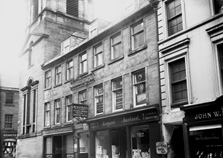 Church Street looking towards Bridge Street. The town clock steeple still exists but the buildings housing McGruther & Marshall and Margaret Macleod Ladies Outfitters are gone, including the alleyway leading to a back entrance of Gellion's Hotel, which is located on Bridge Street. The site is now occupied by Fife Country. The building on the far right is now McEwens of Perth. The clock steeple was erected beside the adjoining Court House and jail in 1791 and rises 45 metres. Gellions is the oldest pub in Inverness, established in 1841.*