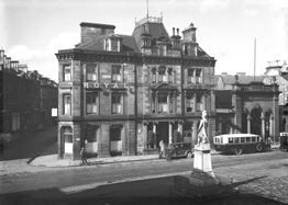 Royal Hotel Inverness, Academy Street, showing vintage car and bus, soldier memorial in Station Square, sunny day. Now occupied by the Clydesdale Bank. Monument to Queen's Own Cameron Highlanders who died in Egypt and the Nile campaign 1882-1887. Made from Portland stone it was unveiled in 1893. December 1930.*