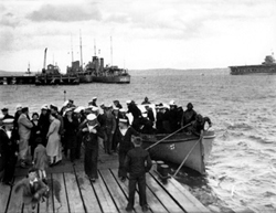 People at Invergordon queuing to take a trip by speedboat to the wreck of the HMS Natal c1932-1938. The H60 was a 'C' Class Destroyer built in 1932 and named HMS Crusader. (She was renamed HMCS Ottawa in 1938). At far right is the aircraft carrier HMS Courageous.*