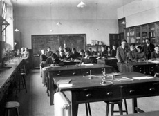 Inverness Royal Academy Science Laboratory, Room 18, High School, 1912. Between 1895-1980 the IRA was located in the Midmills building, currently the UHI-Inverness College (2013). The classroom scene was photographed at the time of the completion of the first extension to the Academy, running along Midmills Road opposite the side entrance to the Crown Church. The accommodation was shared in the early years with Inverness High School, when that school occupied the building which now houses the Crown School, only a short distance away. Accommodation included rooms for science and art, with a gymnasium and these are 'posed' publicity shots. This image was captioned Science Lab 2 in the Highland Times, 2nd July 1914. (Courtesy Inverness Royal Academy Archive IRAA_052).