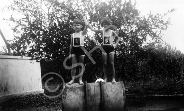 Series of images dating from September 1932 where the children are deep-etched from photographs and inserted into new illustrated backgrounds. The text on the rear of the original photo reads: 'See Viv's head popping up at the back! She's acting as a stone to prevent the drum from rolling.' #