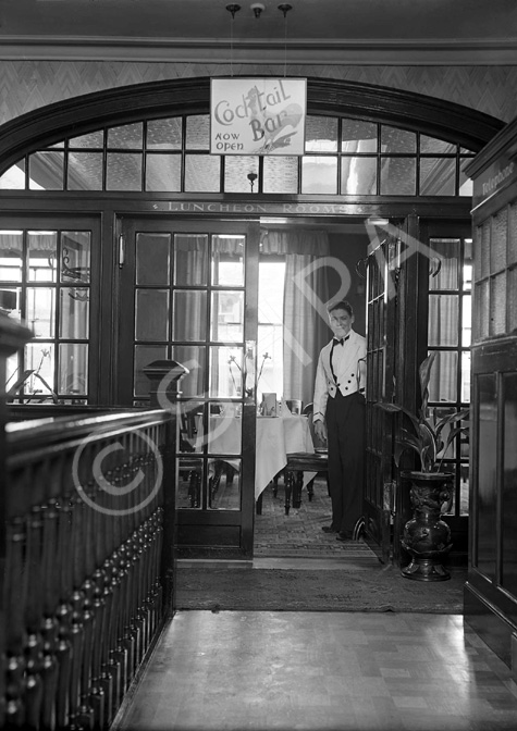 Waiter welcoming into the Luncheon Rooms inside the Carlton Restaurant, with sign pointing to Cocktail Bar upstairs. The cocktail bar opened in May 1936. * 