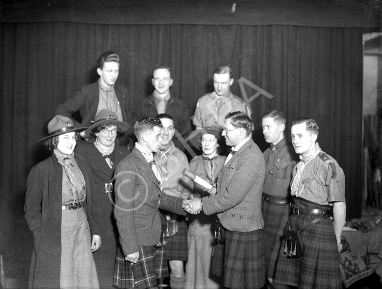 Scout ceremony. Dated c1930s and possibly taken in the since demolished Little Theatre at the top of Raining Stairs on Ardconnel Street, Inverness. The female adults are leaders of what was then called Wolf Cubs (under 11s) - the junior part of Scouting at that time. Man holding scroll appears in image H-0078. #